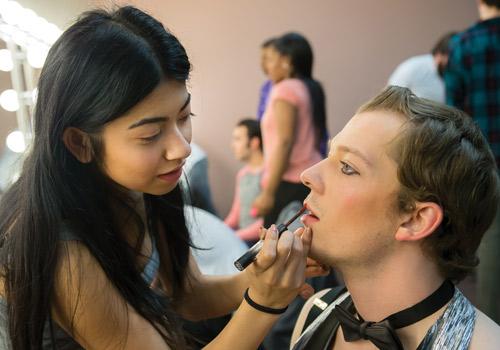  Theatre student Gabby Shaikh finishes stage makeup for fellow student and emcee Corbin George. Photo by Woody Myers