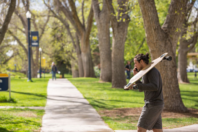 Student with longboard walks campus and talks on the phone