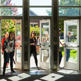 Students walk through three doors in a building on campus