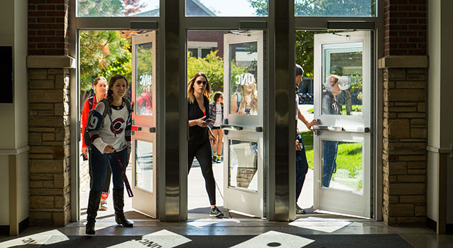 Students walk through three side-by-side glass doors on campus