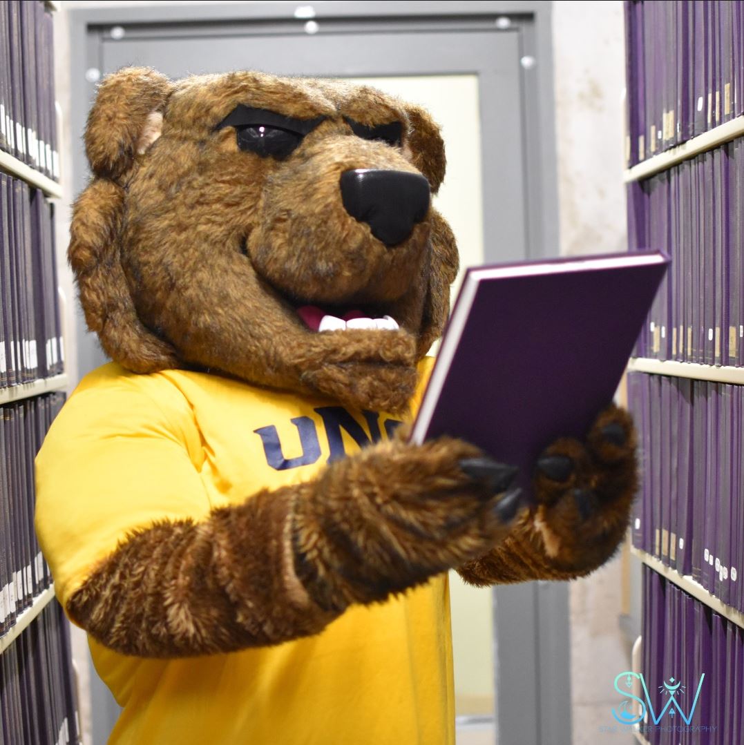 UNC mascot Klawz browsing the stacks of archived dissertations at University Libraries.