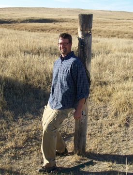 Michael Schiebout in an open field leaning against a fence post. 