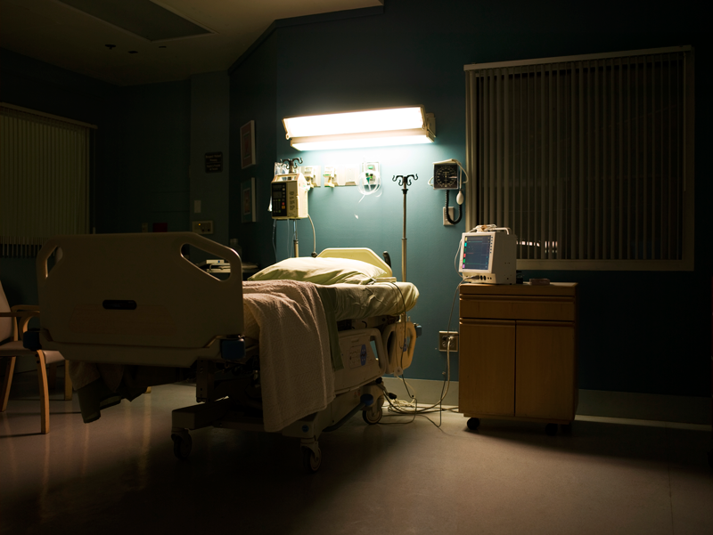 Darkened hospital room with light on over bed