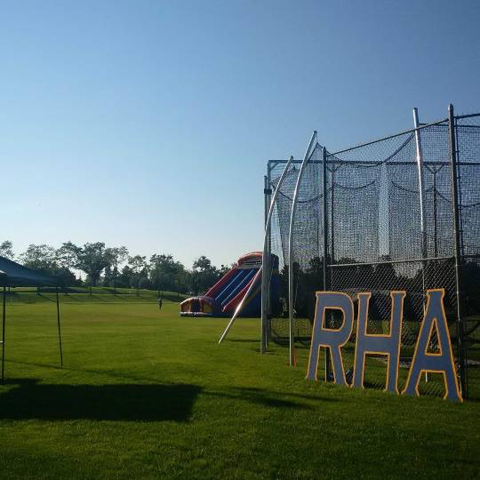 Blue RHA letters leaning agains a fence with an inflatable slide in the background