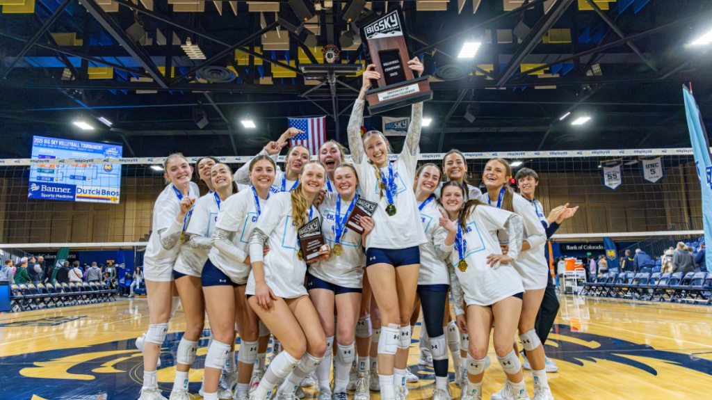 The UNC Volleyball team standing in a group, smiling and holding up a Big Sky trophy