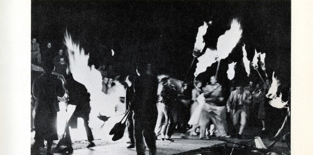 People holding up brooms with fire on them