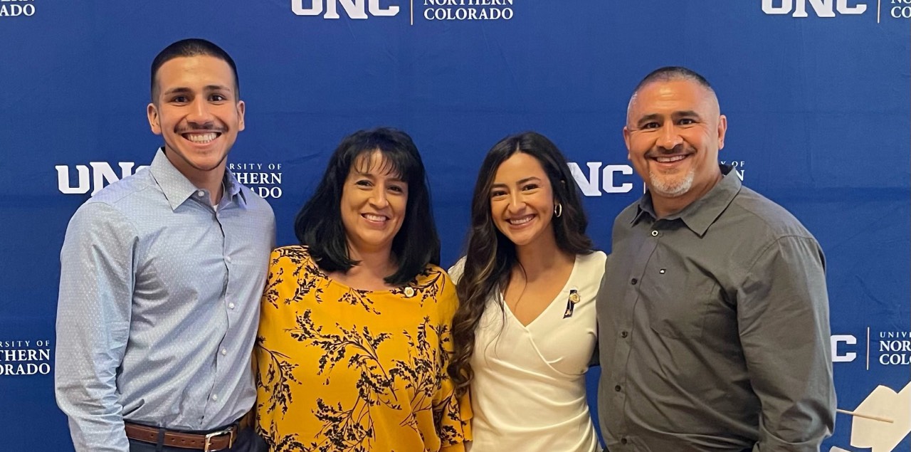 Niko Antuna, Amy Antuna, Kianna Perez, and Kevin Antuna smile in front of a UNC backdrop