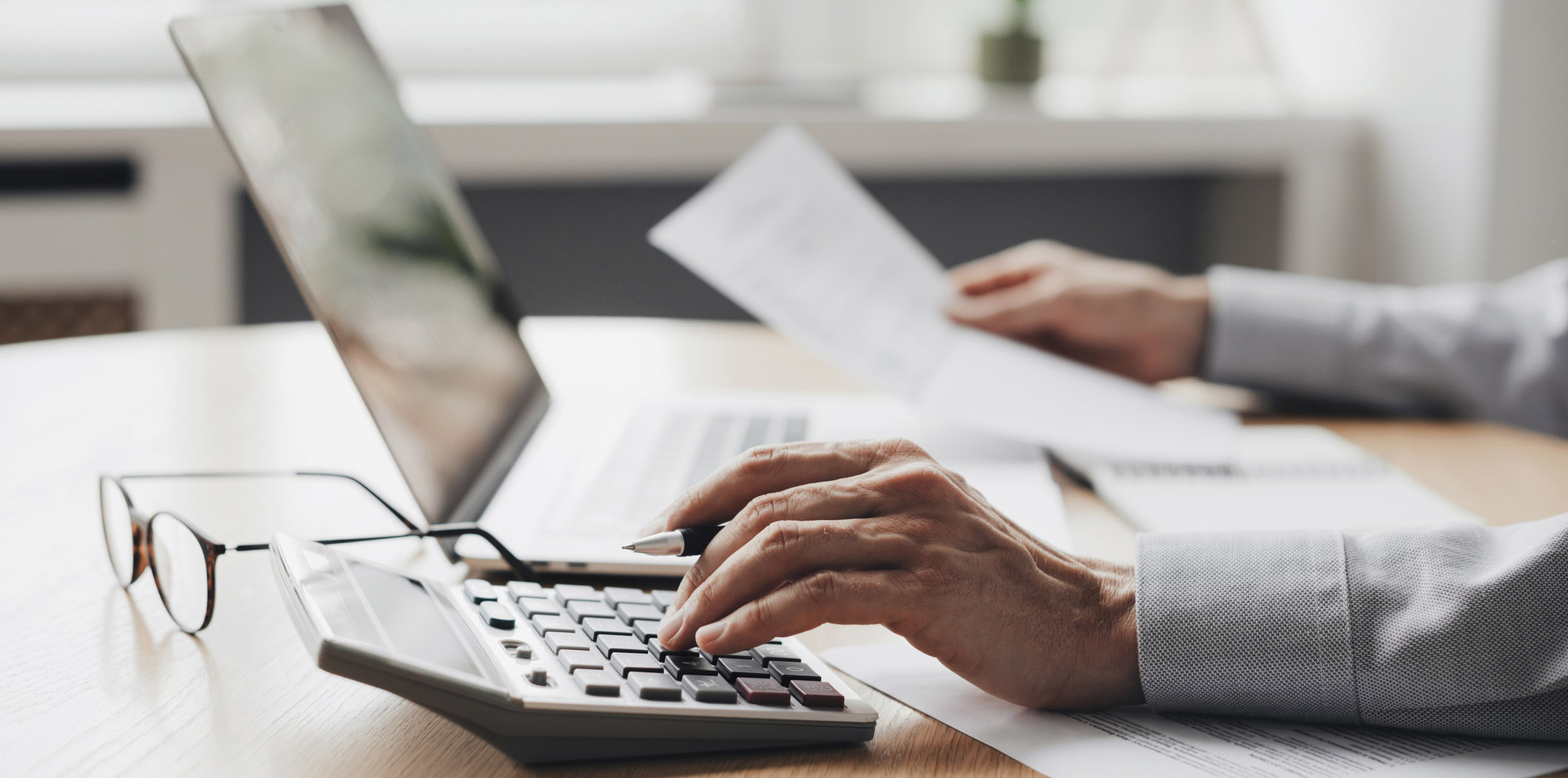 Hand types on calculator while the other holds a paper.