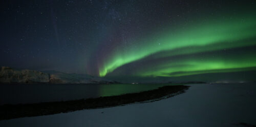 Wavy, glistening green lights in a dark sky above a Norwegian city.