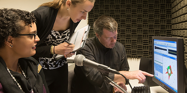 two students in an audiology lab with a professor looking at a computer