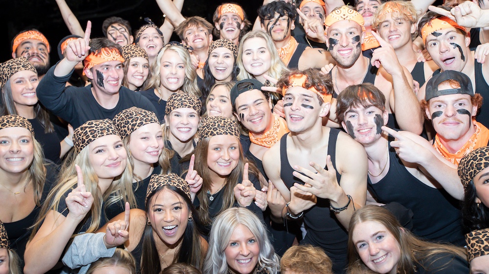 A large number of students wearing black and orange huddled together smiling