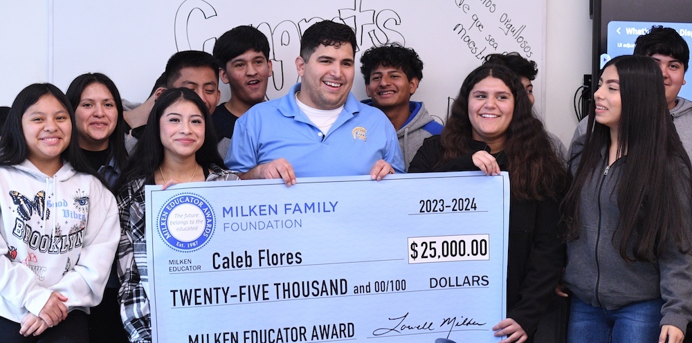 Caleb Flores holding up a big check with his students standing behind him