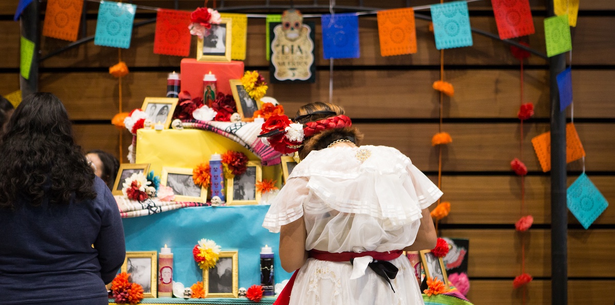 student standing in front of an altar with colorful flags and photographs