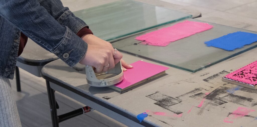 Catherine Cummings helping participants make a block print card by showing them the process it takes to make a block print.