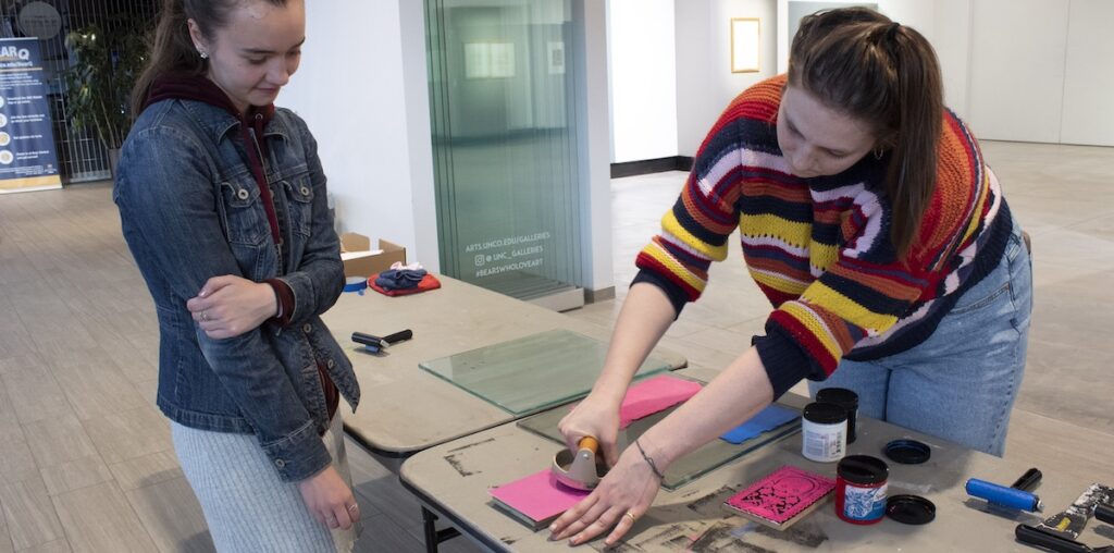 Catherine Cummings helping participants make a block print card by showing them the process it takes to make a block print.