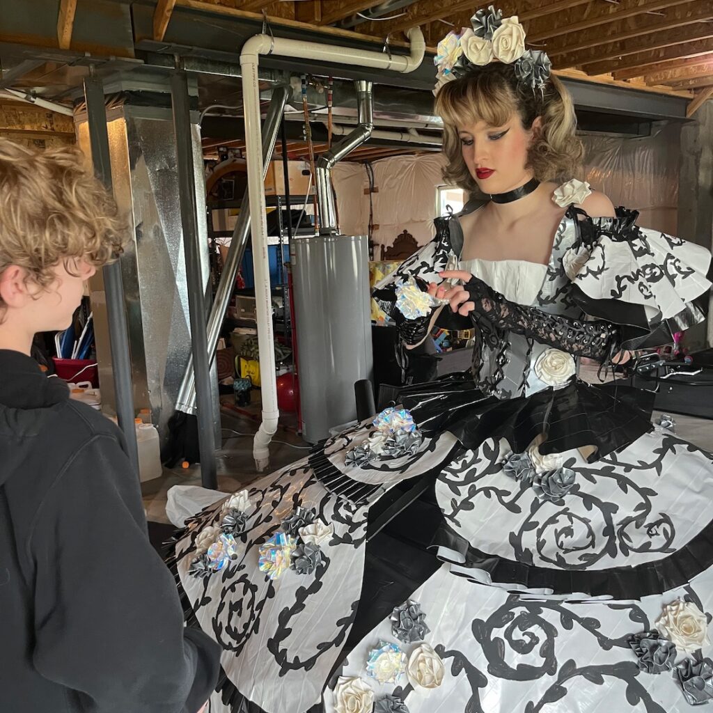 Victoria wearing a black and white dress made of duct tape in a basement