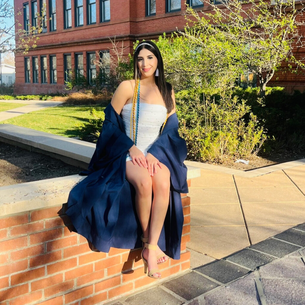 Emily Vega sitting on a brick wall in a cap and gown