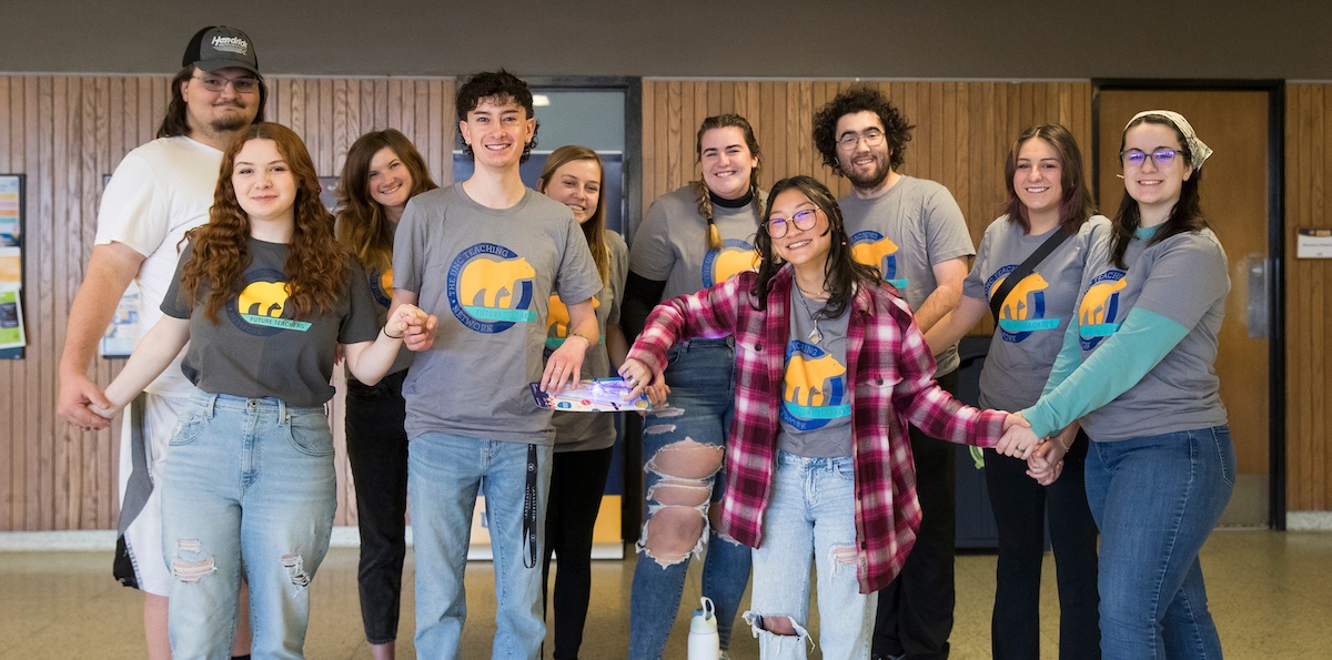 A group of various students wearing the same shirt smiling at the camera.