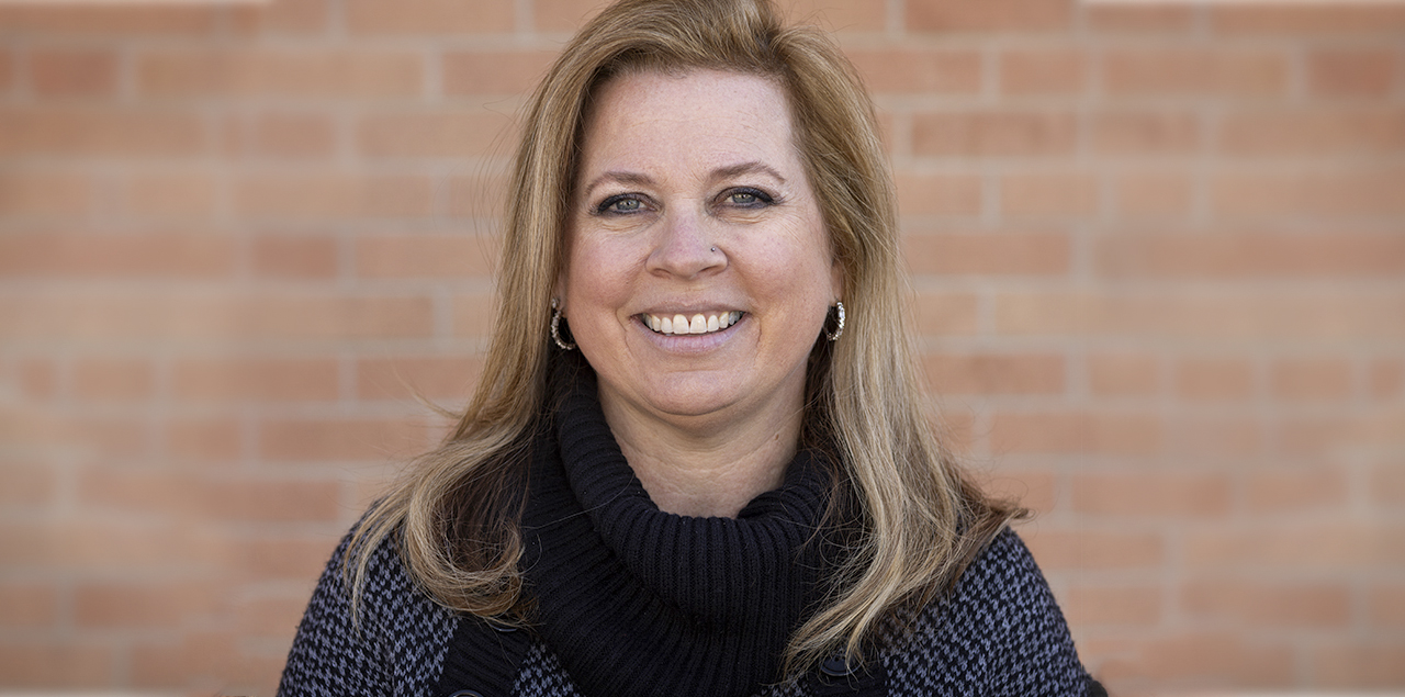 Jessica May smiling at the camera standing in front of a brick wall