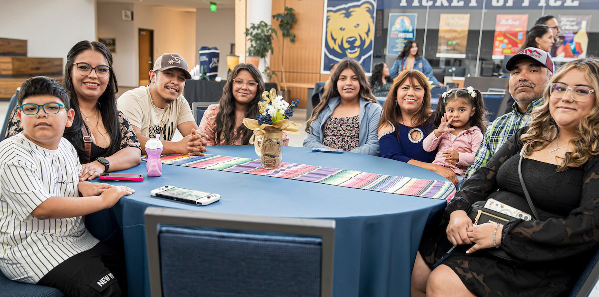 family siting on a table with blue tablecloth, at the back the bear of UNC called Klawz