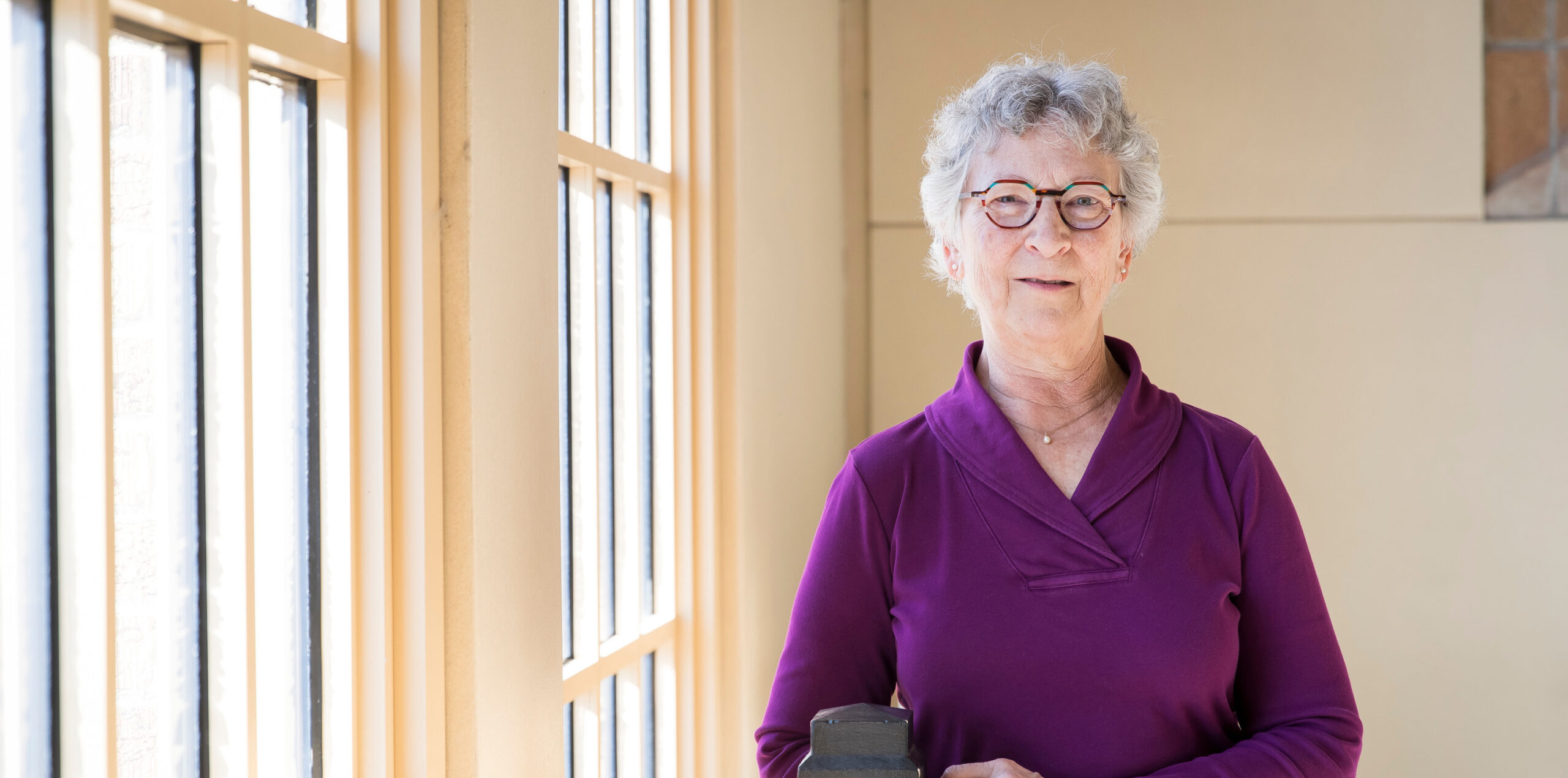 Liz Kissell leaning on a railing near windows smiling