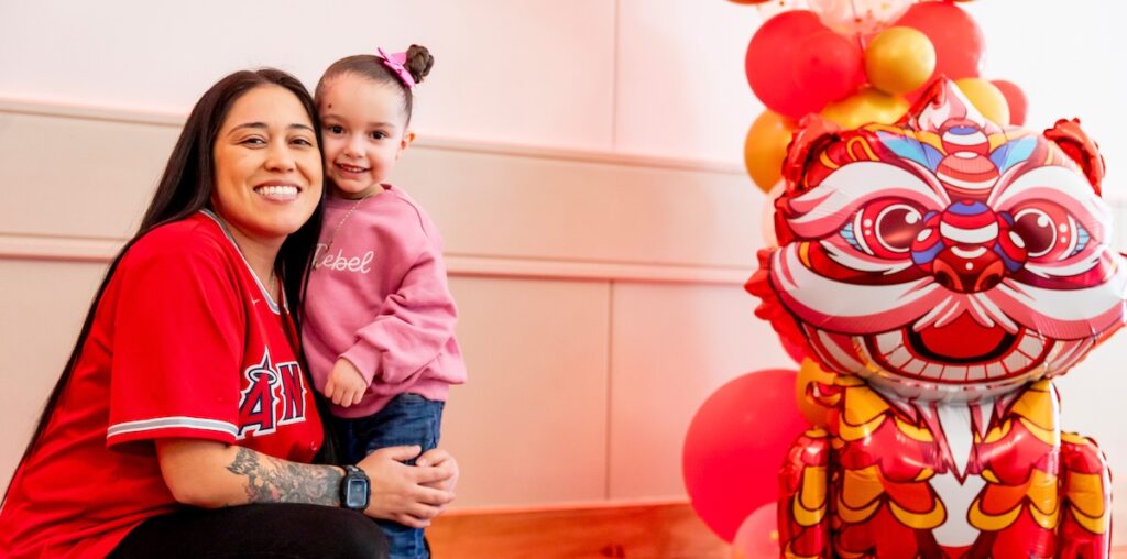 A mom smiling while crouching down to pose with her daughter
