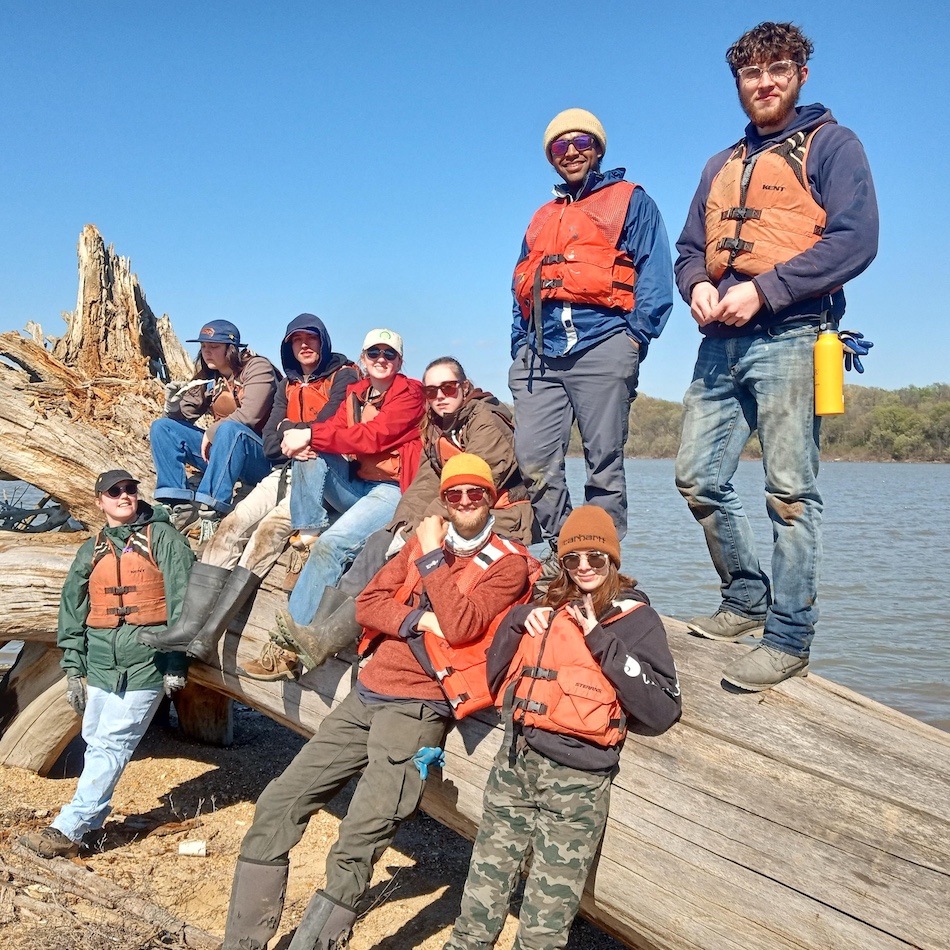 UNC students leaning against a large tree limb near the Mississippi River