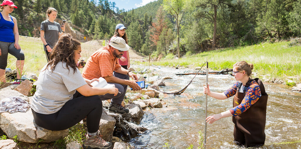 A group of students and a professor in a river collecting data