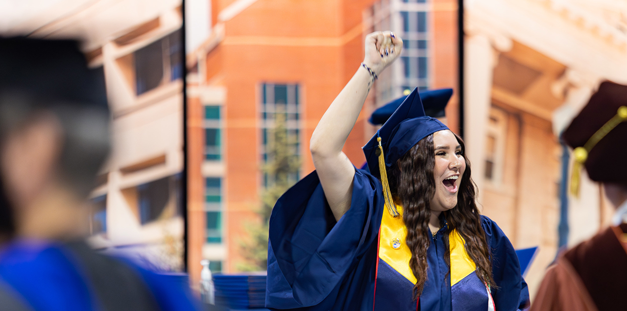 UNC graduate raising their arm and smiling during a graduation ceremony.