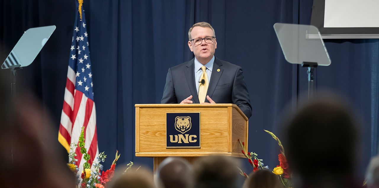 Andy Feinstein standing at a podium on stage addressing a crowd.
