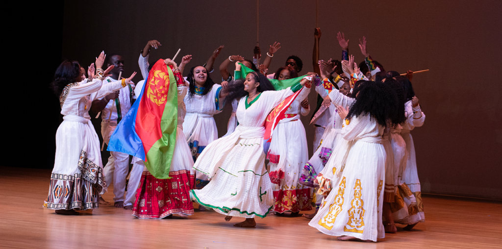A large group dancing together with flags on a stage