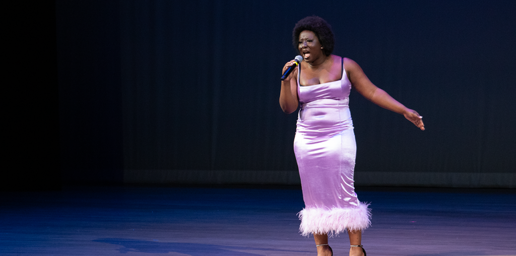 A woman wearing a purple dress singing on stage