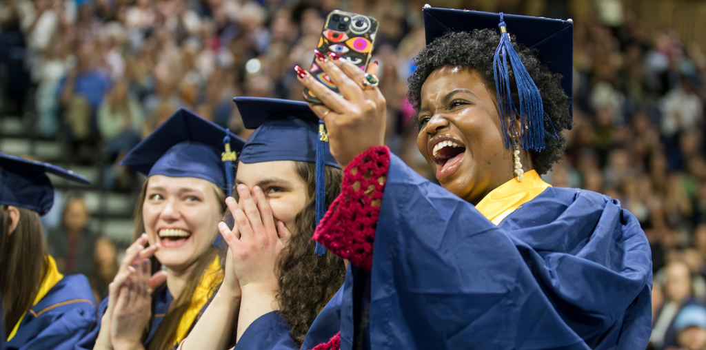 Three graduate students smiling in their cap and gown.