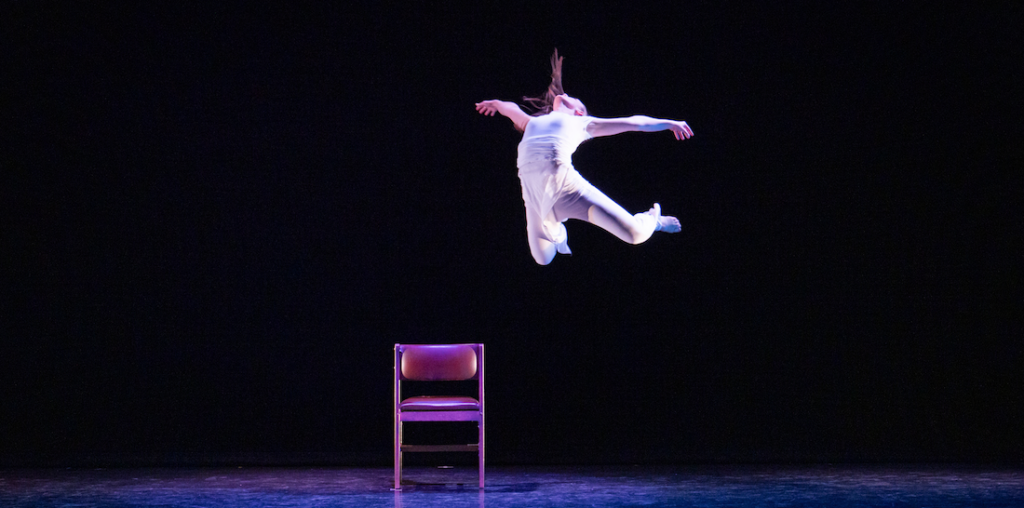 A student dancing leaping into the air above a chair.