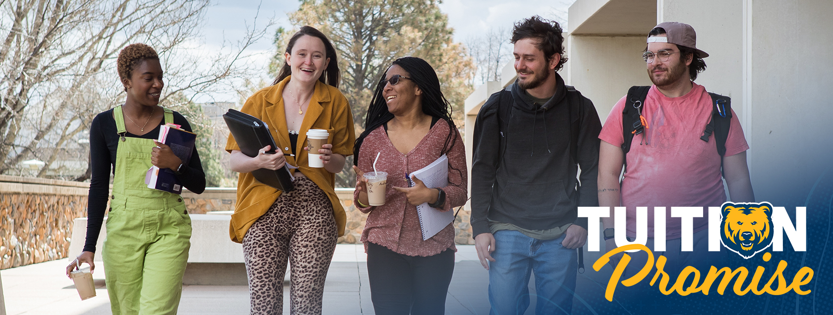 A group of students walking next to each other on the sidewalk smiling