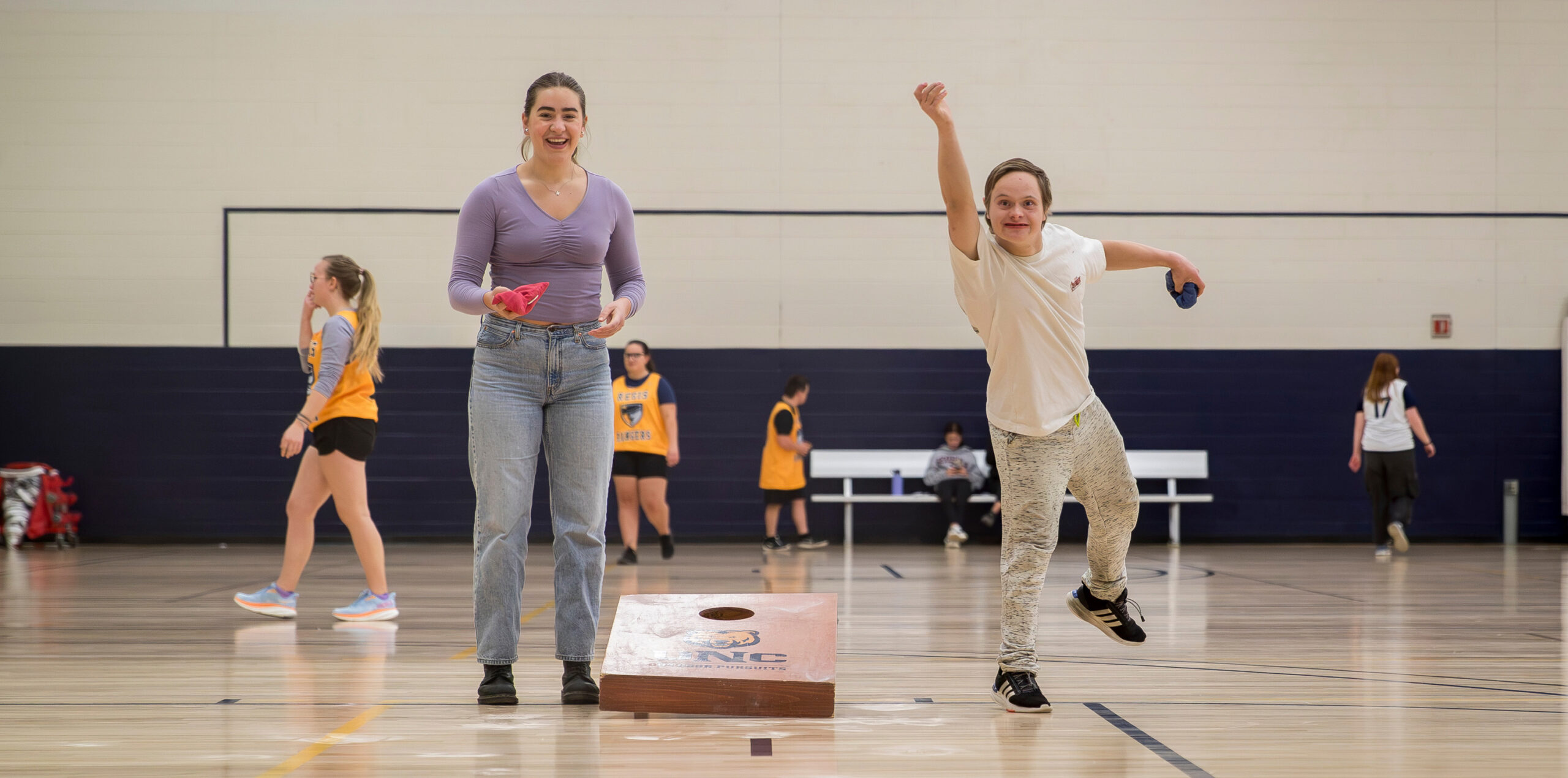 Two people standing next to each other, one is tossing a bag