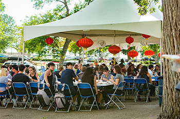 A group of people sitting a canopy with tables and chairs set up for an event celebrating.