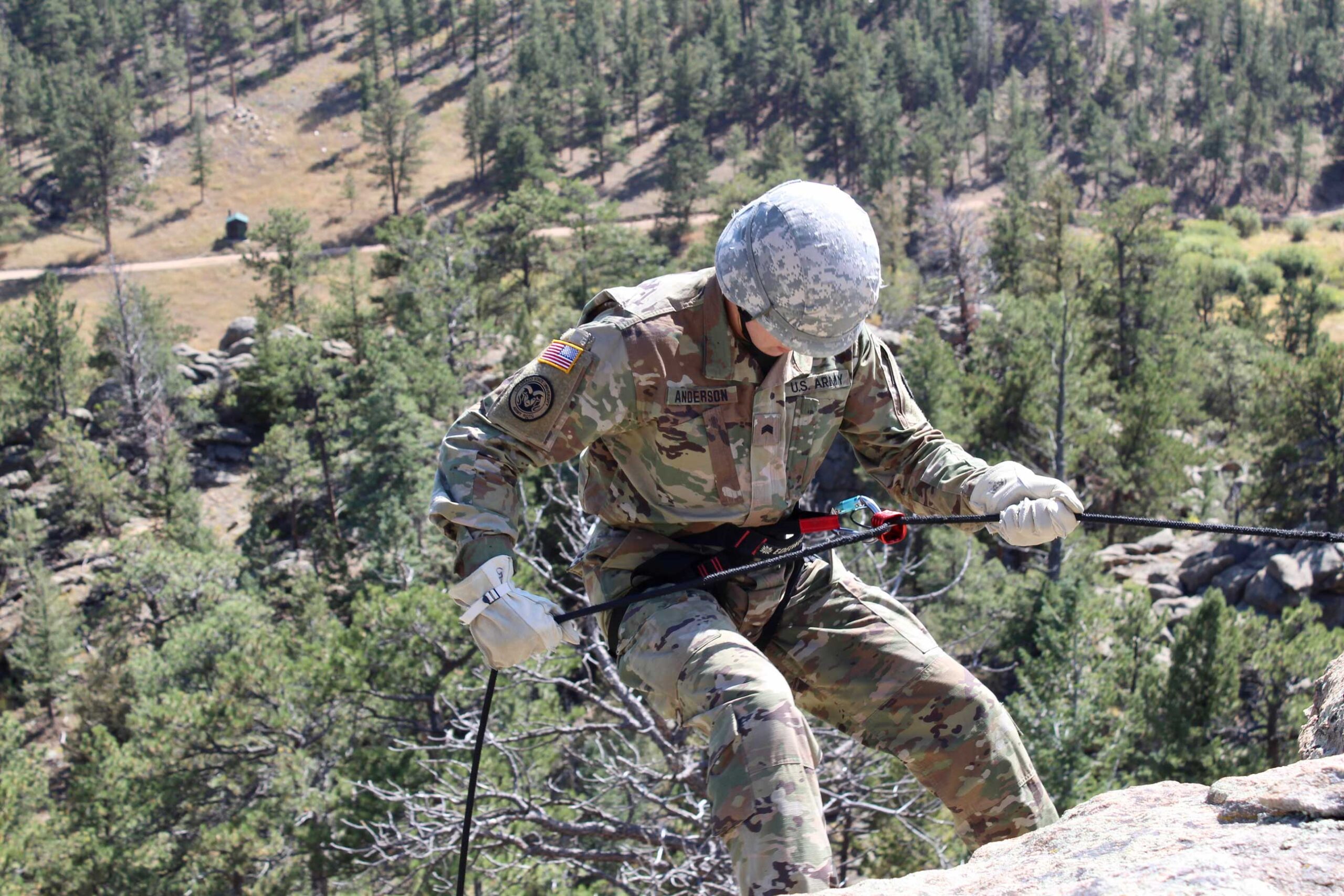 An army personnel wearing a harness as they rappel down a cliff.