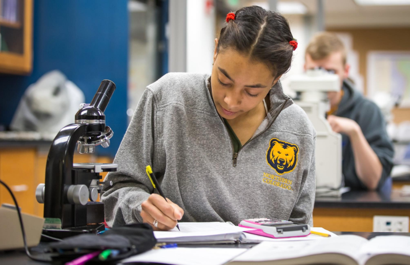 A student using a microscope and taking notes.