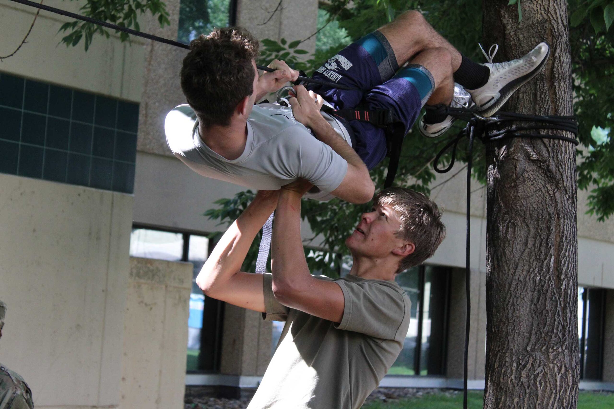 A man holding another man up as he learns to horizontally scale a rope.