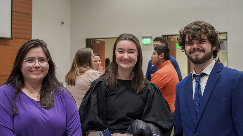 Three students dressed in professional clothing smiling and posing together at Career Conversations event.