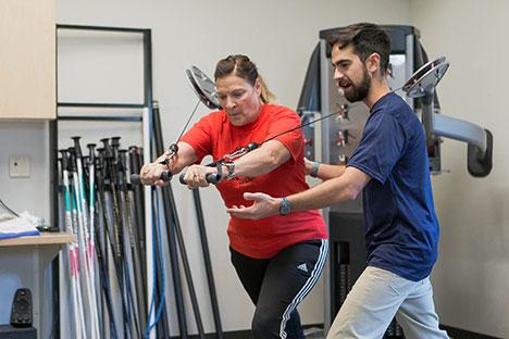A client working out on a cable machine with a trainer.