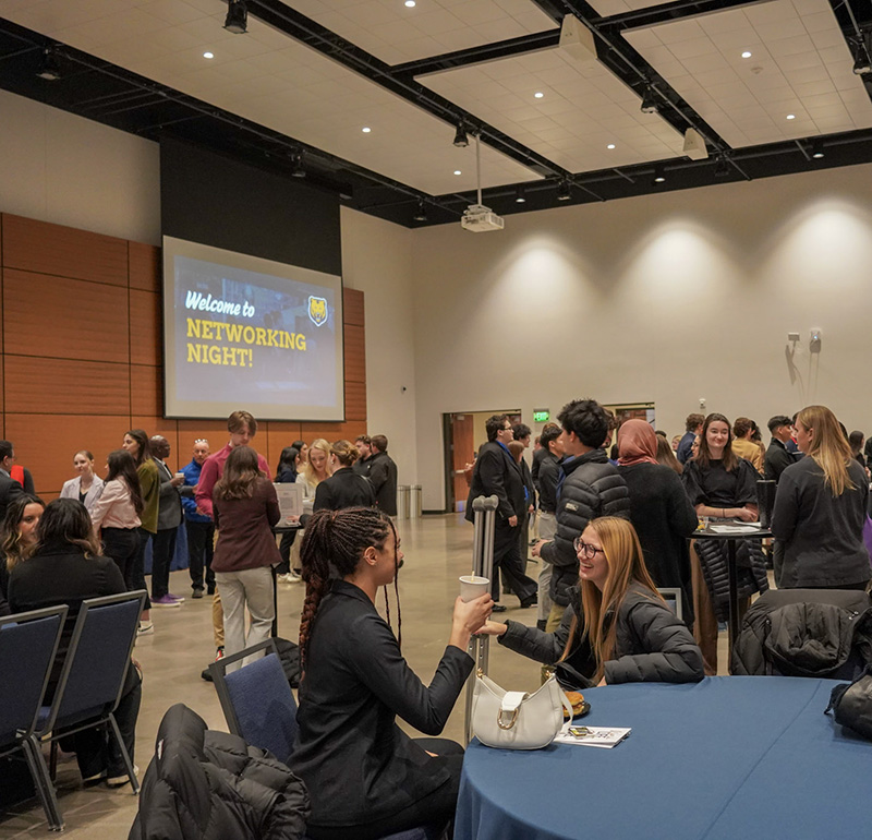 Students networking and engaging in conversations at Networking Night in a large conference room, with a welcoming 