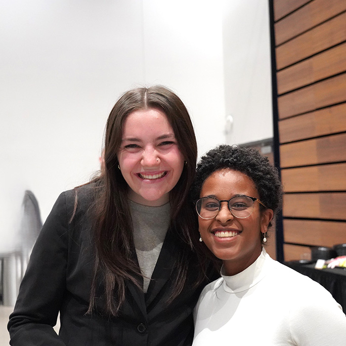 Two female students smiling, dressed in professional attire, standing against a white background.