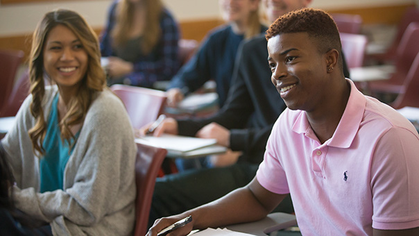 Two students smiling and engaging in a discussion during a professional event in a classroom or conference room setting.