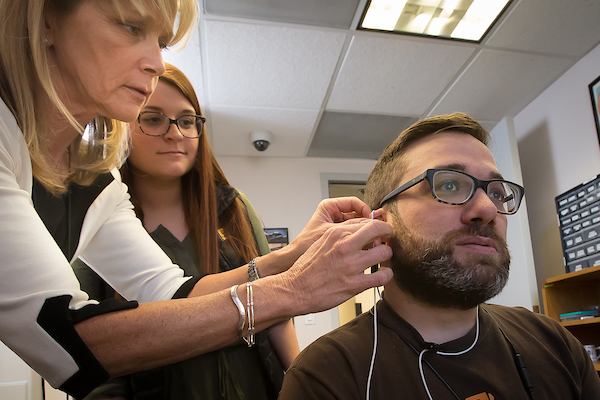 A clinician performs a hearing test on a patient at the UNC Speech-Language Pathology and Audiology Clinic, using professional audiology equipment.
