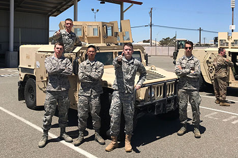a group of cadets posing in front of a military vehicle. 