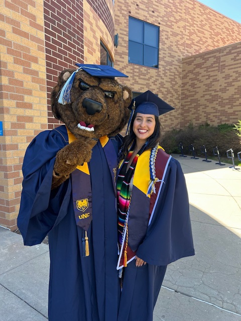 Student graduating talking a picture next to UNC's mascot Klawz.