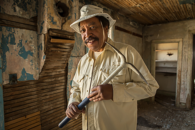 George Junne, holding a pickaxe in an old home.
