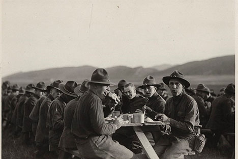 A photo of multiple cadets in mixed military uniforms sitting and eating outside.